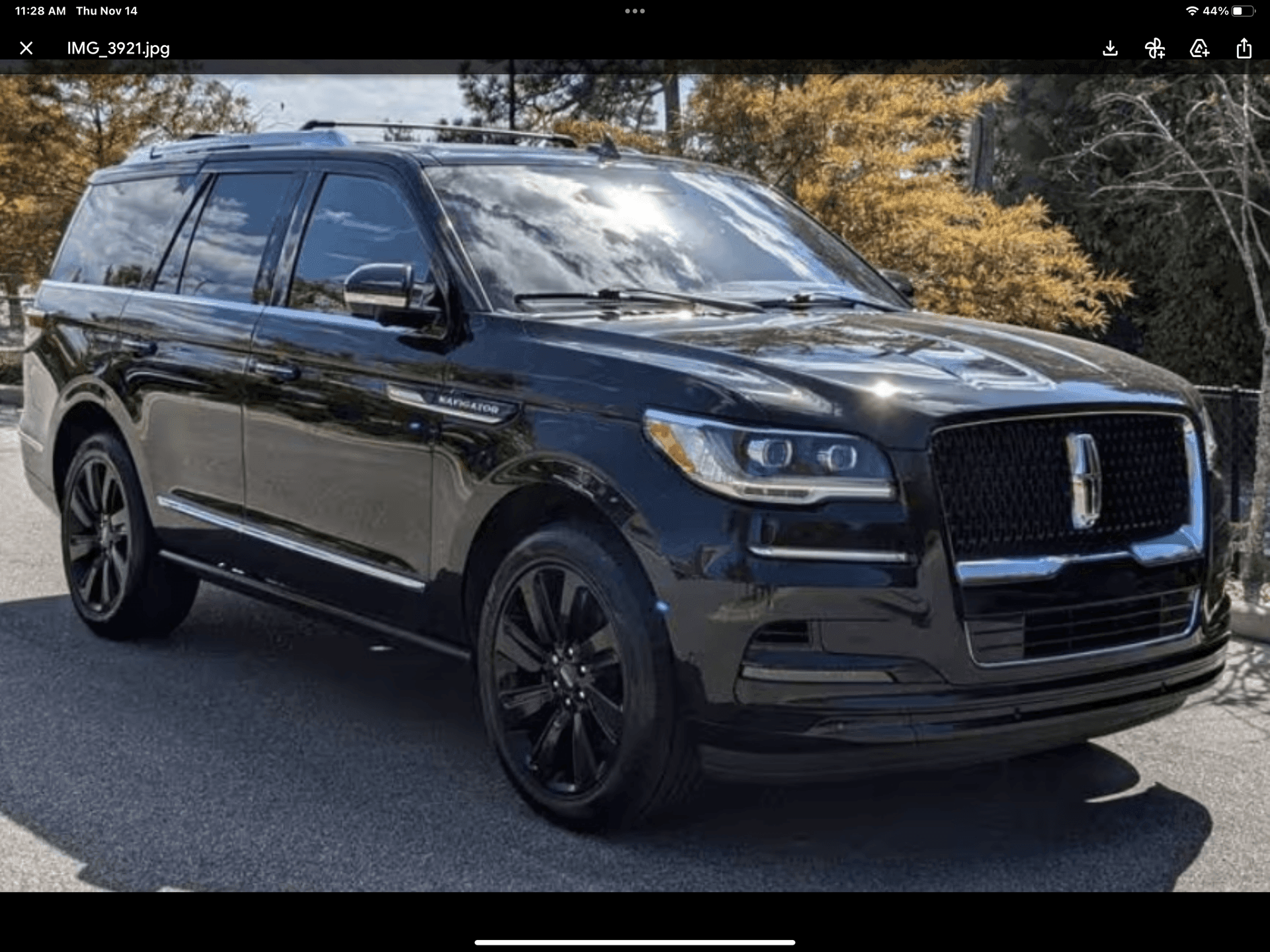 Black luxury SUV parked on a road, surrounded by trees with autumn-colored leaves.